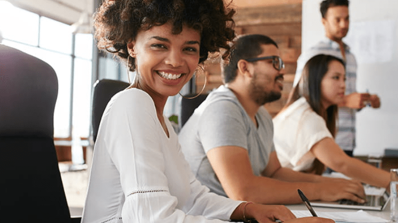 Un groupe de personne travaille et une dame nous regarde en souriant deux salariés en formation avec un expert International SOS